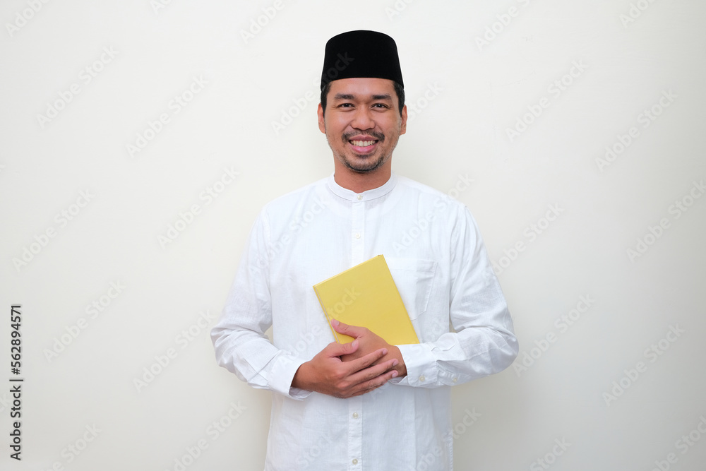 Moslem Asian man smiling at the camera while holding a book Moslem Asian man smiling at the camera while holding a book