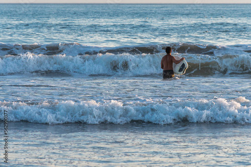 Young man entering the sea with a surfboard.
