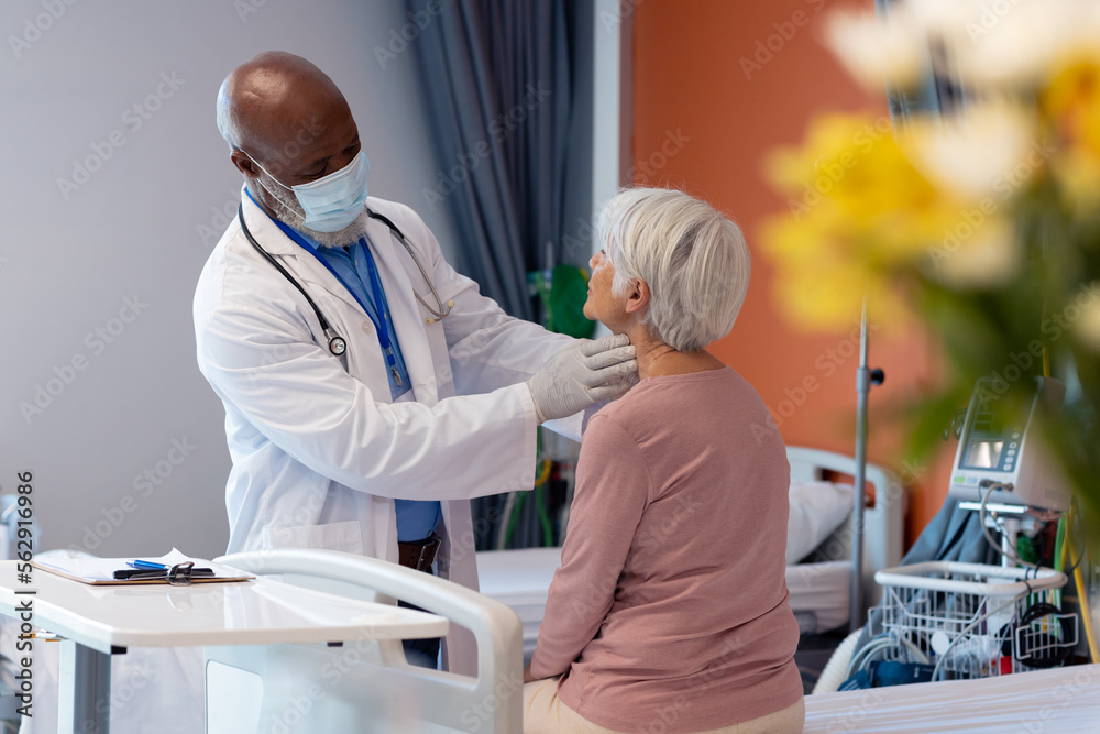 Obraz premium Diverse senior male doctor in face mask examining the throat of senior female patient, copy space