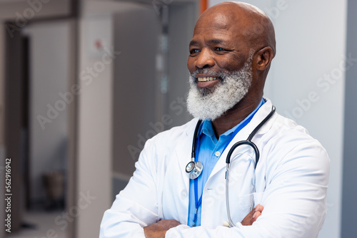 Smiling african american senior male doctor standing in hospital corridor, copy space