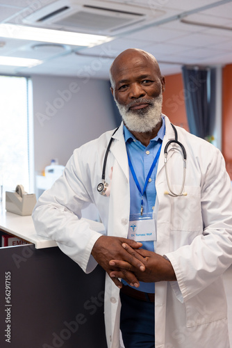 Vertical portrait of smiling senior male doctor with cancer ribbon in hospital ward, copy space