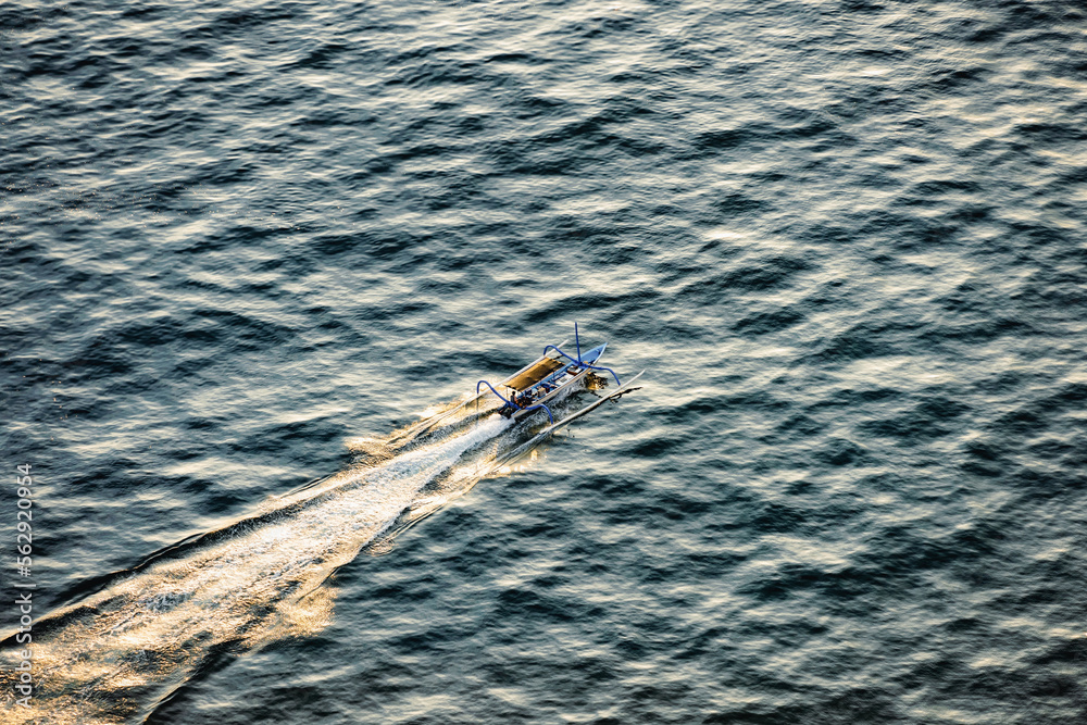 View from above, stunning aerial view of a Jukung canoe sailing at sunset. Nusa Penida, Indonesia. A Jukung is a small wooden Indonesian outrigger canoe.