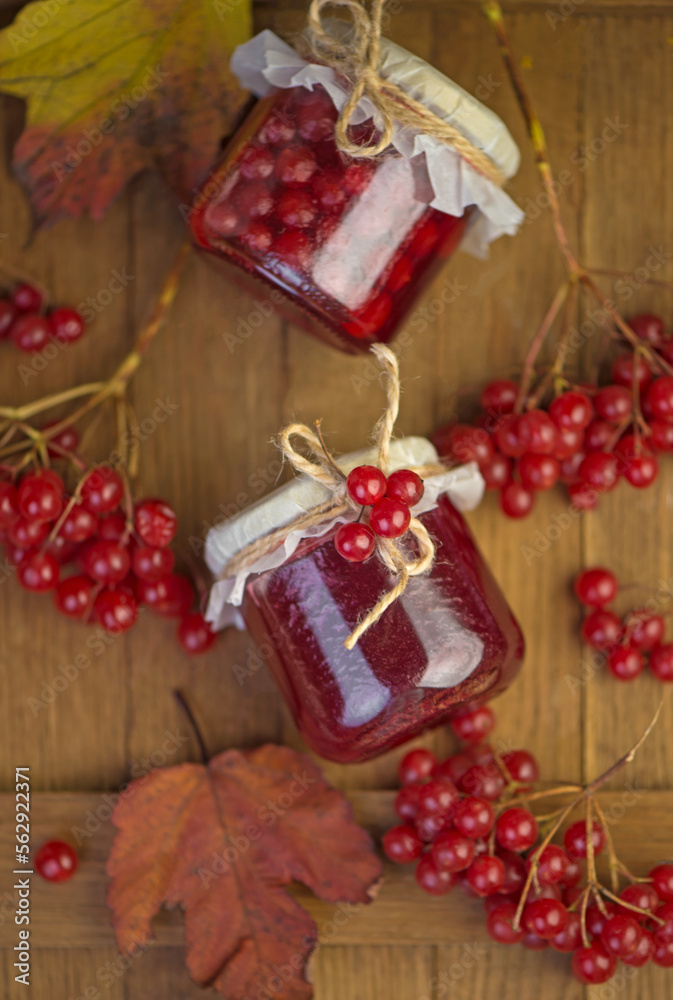 Viburnum fruit jam in a glass jar on a wooden table near the ripe red viburnum berries. Source of natural vitamins. Used in folk medicine. Autumn harvest.