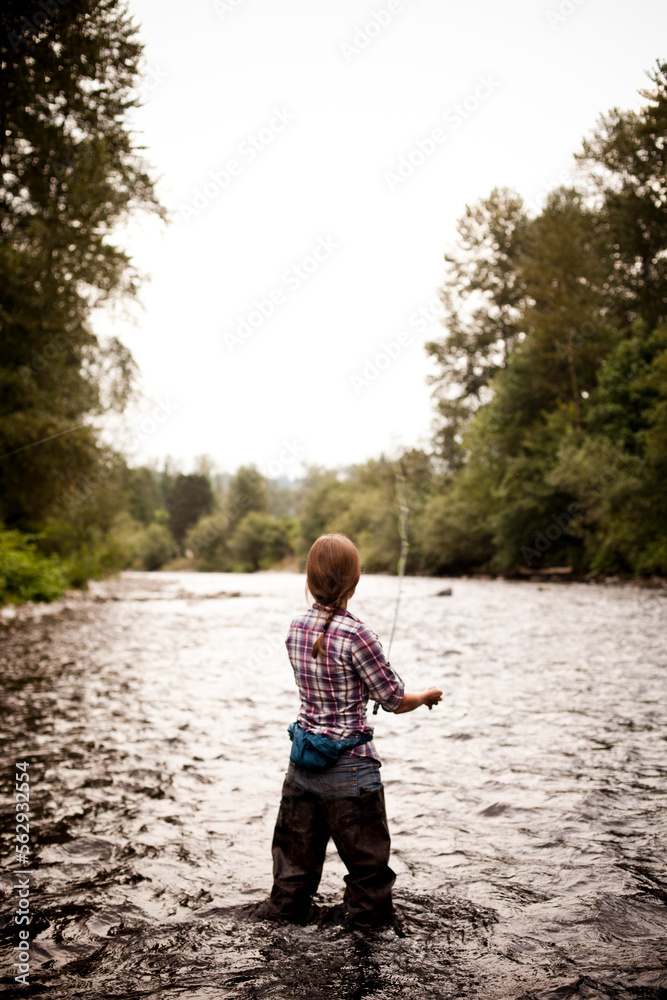 A young woman fly fishes in a river on a clear evening at dusk. A young woman fly fishes in a river on a clear evening at dusk.