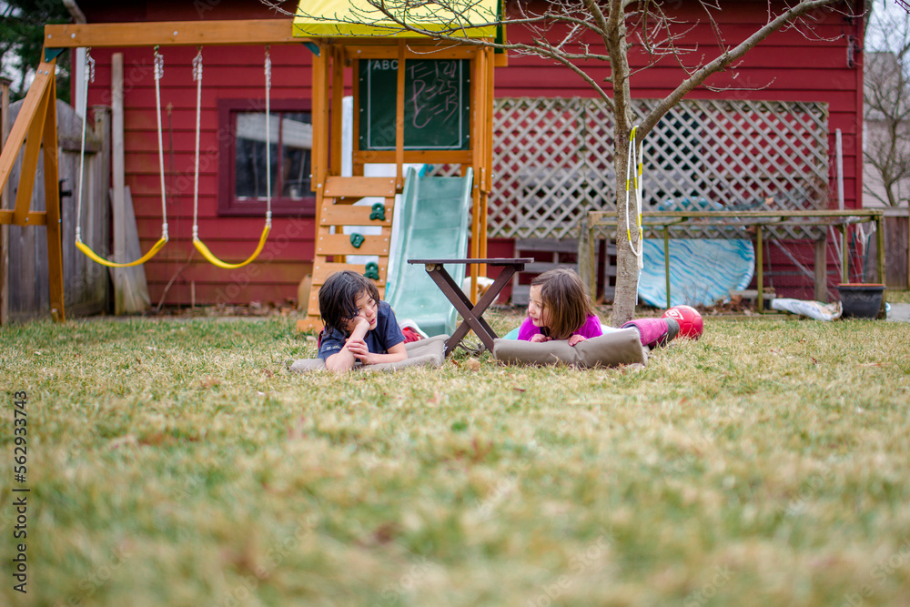 Two happy children lay on mats in their yard chatting together Two happy children lay on mats in their yard chatting together