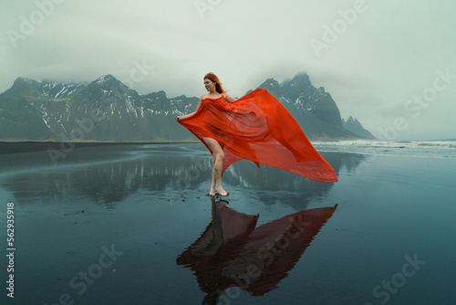 Attractive model in red dress on Reynisfjara beach scenic photography. Picture of person with hills on background. High quality wallpaper. Photo concept for ads, travel blog, magazine, article