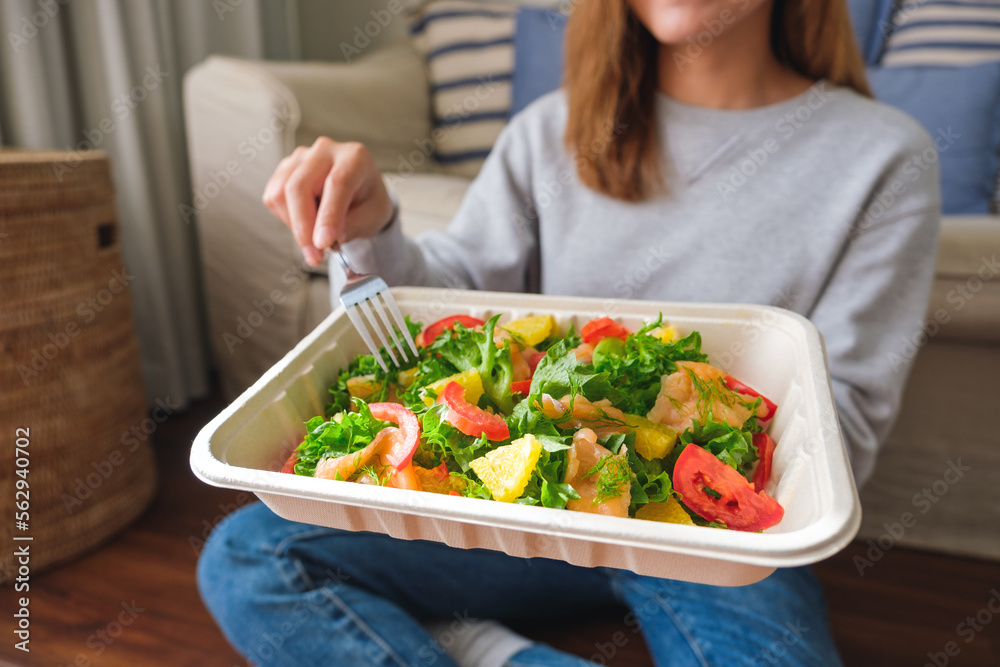 Closeup image of a young woman eating salad in paper box for takeaway food at home Closeup image of a young woman eating salad in paper box for takeaway food at home