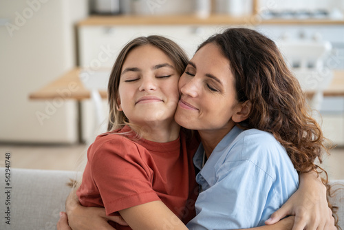 Friendly happy woman and teen girl hug and rejoice at meeting after long separation or going on vacation. Closeup smiling positive mother and daughter hugging each other tightly sits on sofa at home