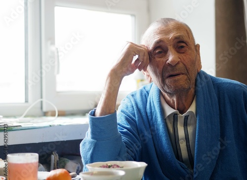 Close up portrait of 92 year old grandfather. Grandpa sits at the table in his room and stares into the camera. Care and everyday life of the elderly.
