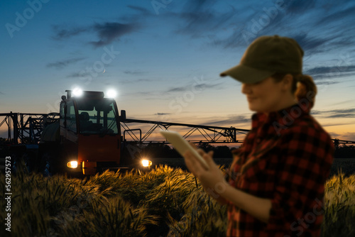 Farmer controls sprayer with a tablet at night. Smart farming and precision agriculture
