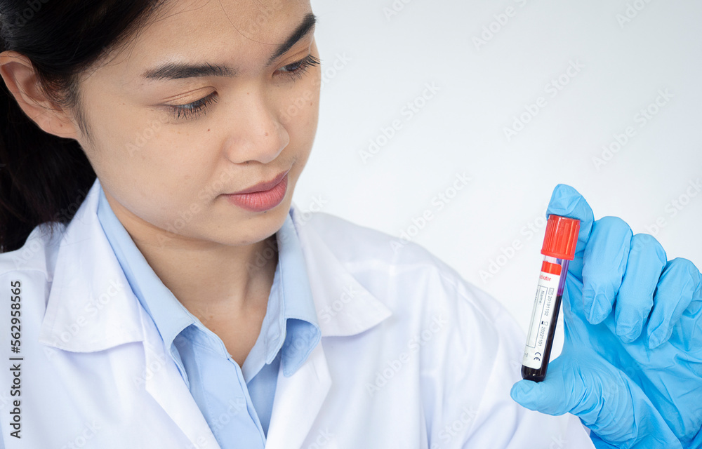 Portrait of beautiful young female in white coat sitting at workplace and working with blood sample Portrait of beautiful young female in white coat sitting at workplace and working with blood sample