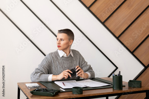 A business woman with a short haircut looks out the window while sitting at her desk in the office