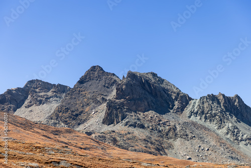 Gentle mountain slope covered with yellow autumn grass in foreground and black impregnable steep sharp rocks in background. Gran Paradiso National Park, Aosta valley, Italy