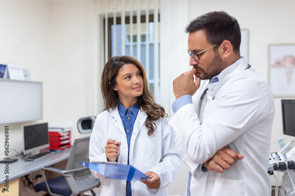 Doctors discussing over a medical report in hospital. Female and male doctor checking clinical report of patient online. Healthcare staff having discussion in a office of private clinic.