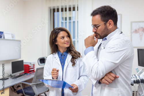 Doctors discussing over a medical report in hospital. Female and male doctor checking clinical report of patient online. Healthcare staff having discussion in a office of private clinic.