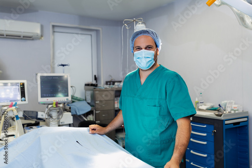Portrait of male surgeon in operation theater looking at camera. Doctor in scrubs and medical mask in modern hospital operating room.