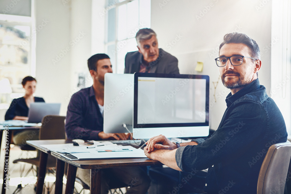 Portrait, mature and business man by computer in office workplace. Planning, pc or confident male employee working on marketing report, advertising proposal or sales project with coworkers in company Portrait, mature and business man by computer in office workplace. Planning, pc or confident male employee working on marketing report, advertising proposal or sales project with coworkers in company
