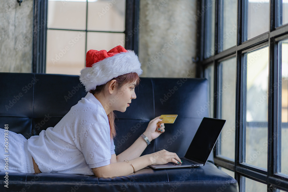 Young beautiful Asian woman in white dress wearing hat smiling and holding bank card to pay laptop for online shopping or doing financial transaction on sofa at home Young beautiful Asian woman in white dress wearing hat smiling and holding bank card to pay laptop for online shopping or doing financial transaction on sofa at home