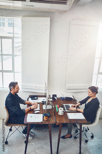 Laptop, computer and business people with opposite desk in office workplace. Planning, strategy and workers, man and woman with computers typing or working on sales, marketing or advertising project.