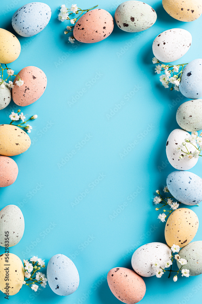 Border with Easter composition with spring flowers and colorful quail eggs over blue background. Springtime and Easter holiday concept with copy space. Top view