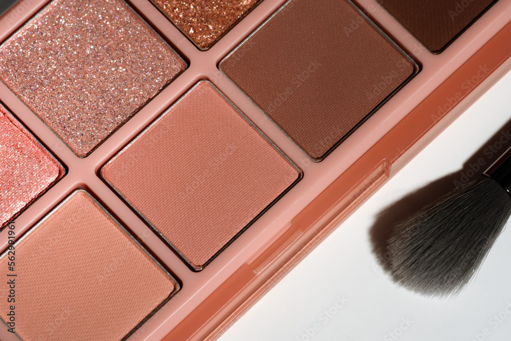 Fototapeta premium Top view flat lay glitter and brown eyeshadow palette and silver makeup brush on white background. Cosmetic banner
