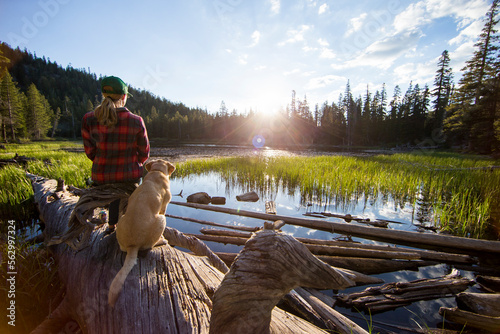 A woman and her dog enjoy the sunset along the shore.