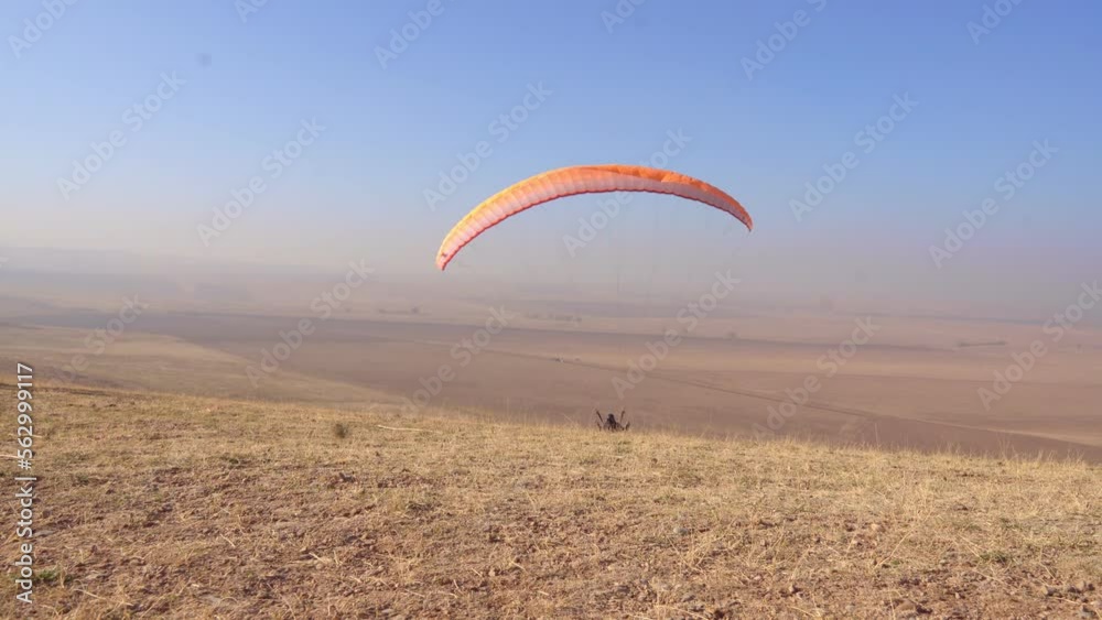 The pilot on the paraglider catches the tailwind, keeps the wing on top, trying to cherish.Above the paraglider there is a blue cloudless sky and autumn fields. The pilot on the paraglider catches the tailwind, keeps the wing on top, trying to cherish.Above the paraglider there is a blue cloudless sky and autumn fields.