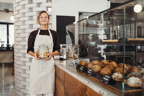 Young female baker entrepreneur standing at the counter of bakery and coffee shop.
