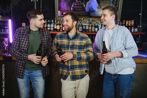 Young men in casual clothes are talking, laughing and drinking while sitting at bar counter in pub