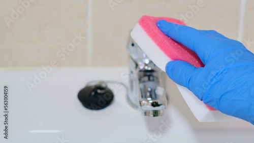 Señora de la limpieza lavando grifo del cuarto de baño con un estropajo y guantes