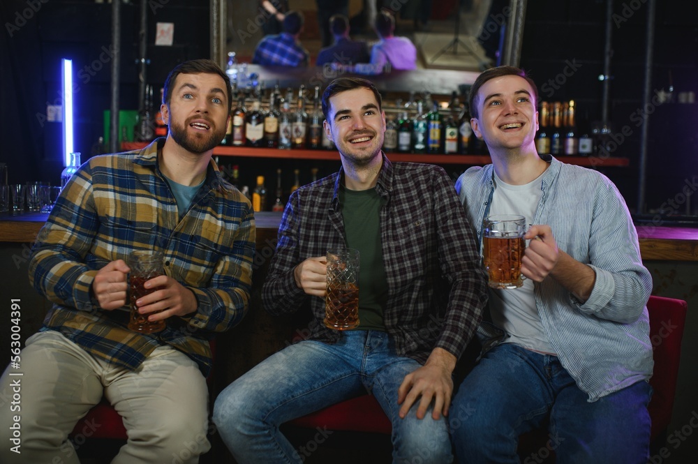Young men in casual clothes are talking, laughing and drinking while sitting at bar counter in pub Young men in casual clothes are talking, laughing and drinking while sitting at bar counter in pub