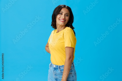 Woman in yellow t-shirt on blue background posing gestures emotions and signals with smile, hands up happiness copy space