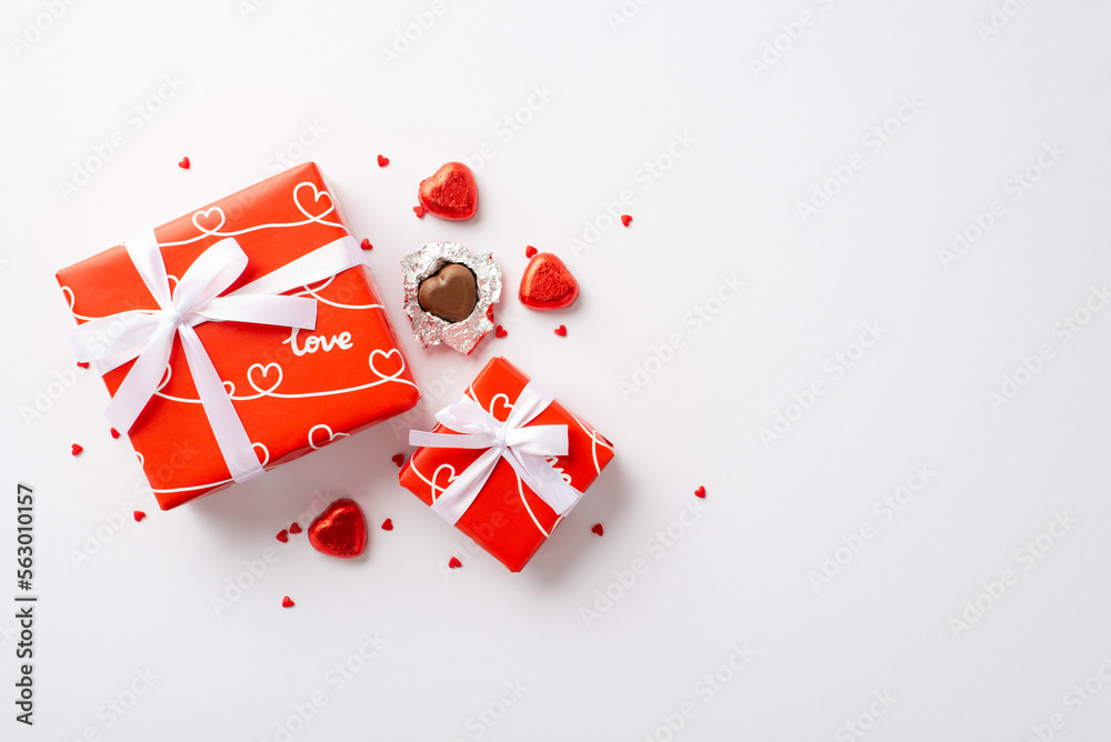 Valentine's Day concept. Top view photo of red gift boxes heart shaped chocolate candies and sprinkles on isolated white background Valentine's Day concept. Top view photo of red gift boxes heart shaped chocolate candies and sprinkles on isolated white background