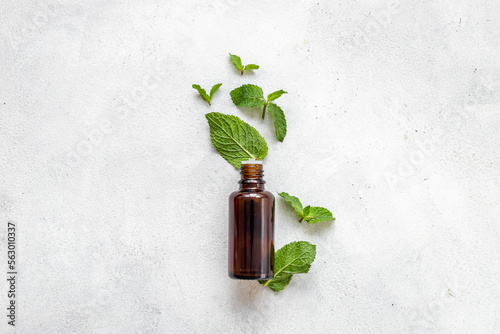 Bottle of essential peppermint oil with fresh green mint leaves