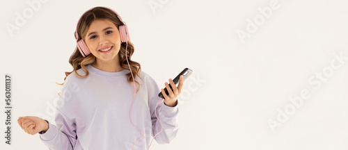 Image of optimistic woman in purple sweetshot holding smartphone while listening to music with headphones isolated over white background © Яна Солодкая