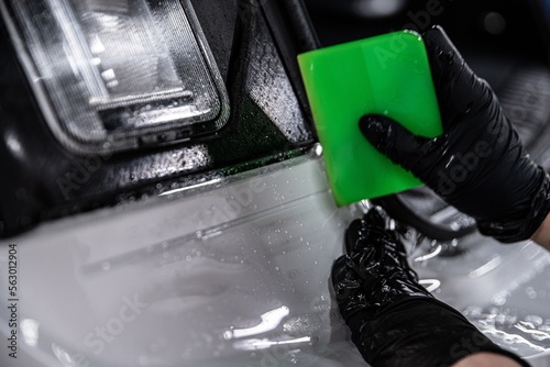 Obraz na płótnie Employee of a car detailing studio applies a colorless protective film covering the paintwork of a white car. The film protects the car paint against UV rays and scratches w salonie