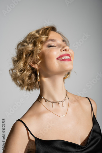 portrait of joyful young woman with closed eyes smiling isolated on grey.