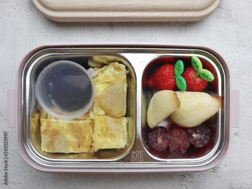 Pempek lenggang or Omelette, sweet sauce, strawberry, snackfruit and grape for simple snack box. Kindergarten school lunch box. Selective focus. Little noise and grainy.  photo