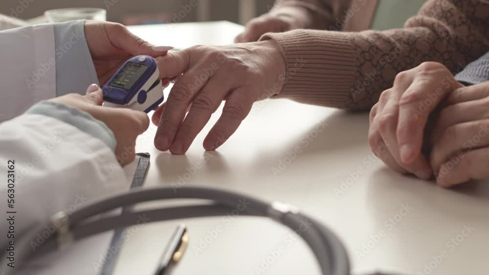 Closeup of unrecognizable female doctor applying pulse oximeter on senior patient finger to measure oxygen saturation of blood during appointment in her office Closeup of unrecognizable female doctor applying pulse oximeter on senior patient finger to measure oxygen saturation of blood during appointment in her office