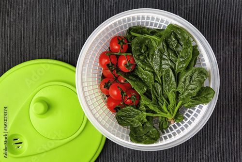 Washed red cherry tomatoes on a branch and green spinach leaves in a centrifuge strainer on a table with a black textile tablecloth photo