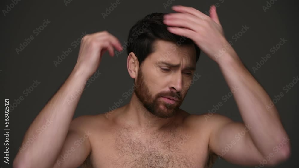 Shirtless brunette man applying hairspray and smiling isolated on dark grey 