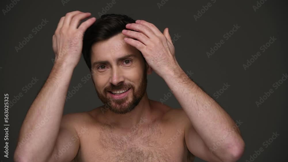 Smiling and shirtless man touching hair and looking at camera isolated on dark grey Smiling and shirtless man touching hair and looking at camera isolated on dark grey