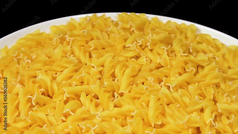 Uncooked Fusilli Pasta on White Plate Rotating against Black Background. Fat and Unhealthy Food. Dry Spiral Macaroni. Italian Culture and Cuisine. Raw Golden Pasta Uncooked Fusilli Pasta on White Plate Rotating against Black Background. Fat and Unhealthy Food. Dry Spiral Macaroni. Italian Culture and Cuisine. Raw Golden Pasta