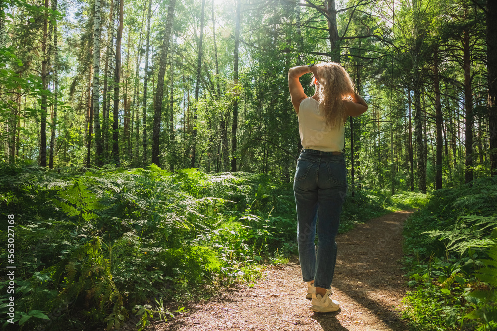 The young woman walks through a dark forest on a sunny day The young woman walks through a dark forest on a sunny day