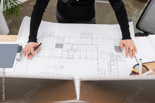 Cropped view of interior designer working with blueprint near devices in office.