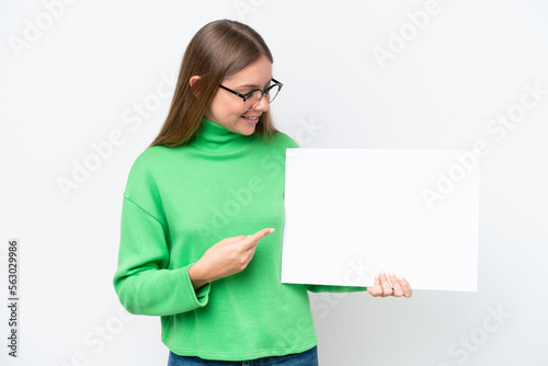 Young caucasian woman isolated on white background holding an empty placard with happy expression and pointing it