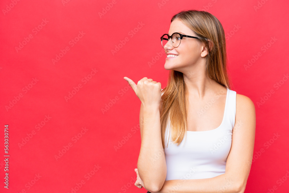 Young beautiful woman isolated on red background pointing to the side to present a product Young beautiful woman isolated on red background pointing to the side to present a product