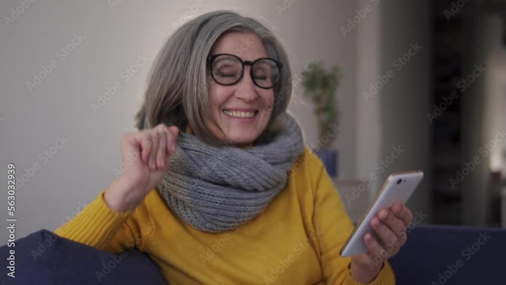 Senior stylish woman enjoying music on smartphone, dancing sitting on sofa Senior stylish woman enjoying music on smartphone, dancing sitting on sofa