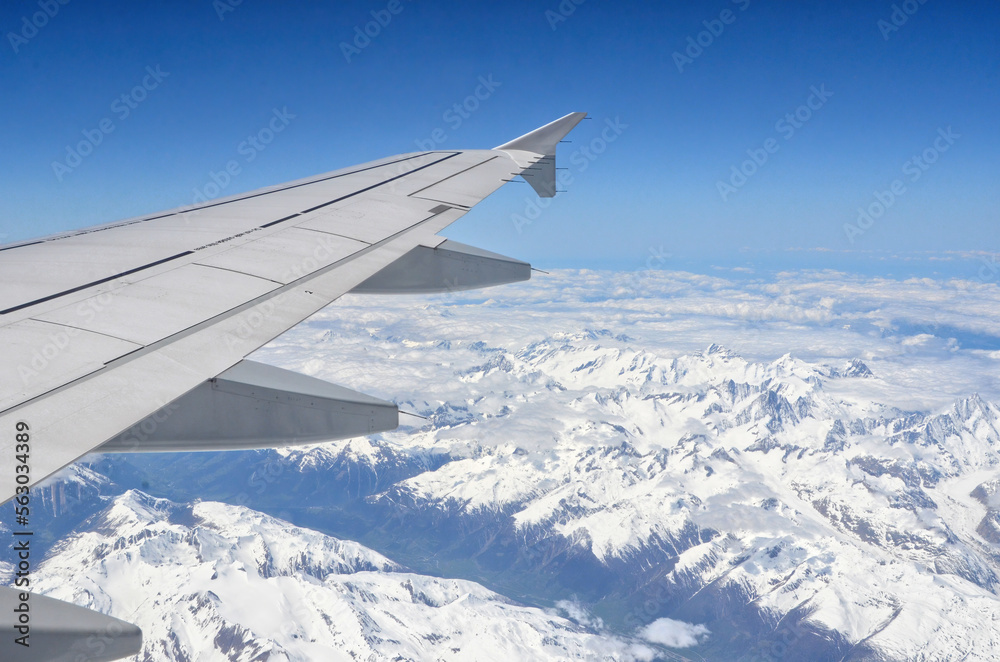Fototapeta premium Wing of a plane flying over snowy mountains