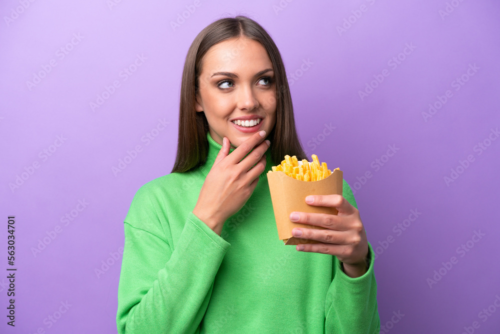 Young caucasian woman holding fried chips on purple background looking up while smiling Young caucasian woman holding fried chips on purple background looking up while smiling